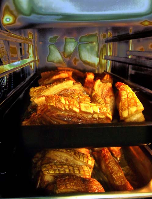 Blick in den Ofen, gefüllt mit zwei Blechen voller Schweineschulterstücke mit röscher Kruste