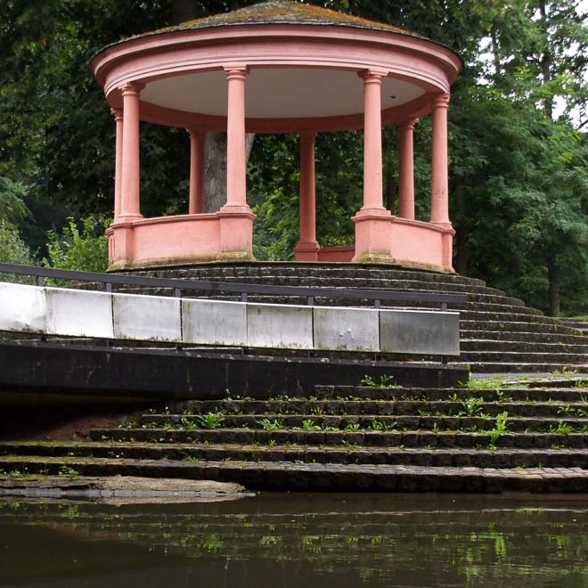 Ein rosafarbenes rundes Pavillon liegt oben an einer runden Treppe und spiegelt sich im darunterliegenden Wasser der Regnitz.