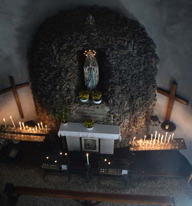 Eine von Natursteinen eingerahmte Marienfigur, auf einem einfachen Altar, wird von dutzenden Kerzen der Wallfahrer beleuchtet.